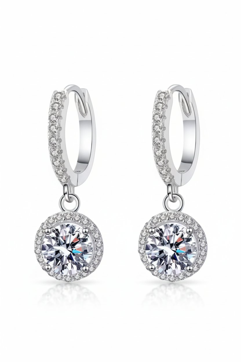 Close-up of The Stella drop earrings featuring a brilliant moissanite center stone in a round pavé halo, suspended from a silver huggie hoop.