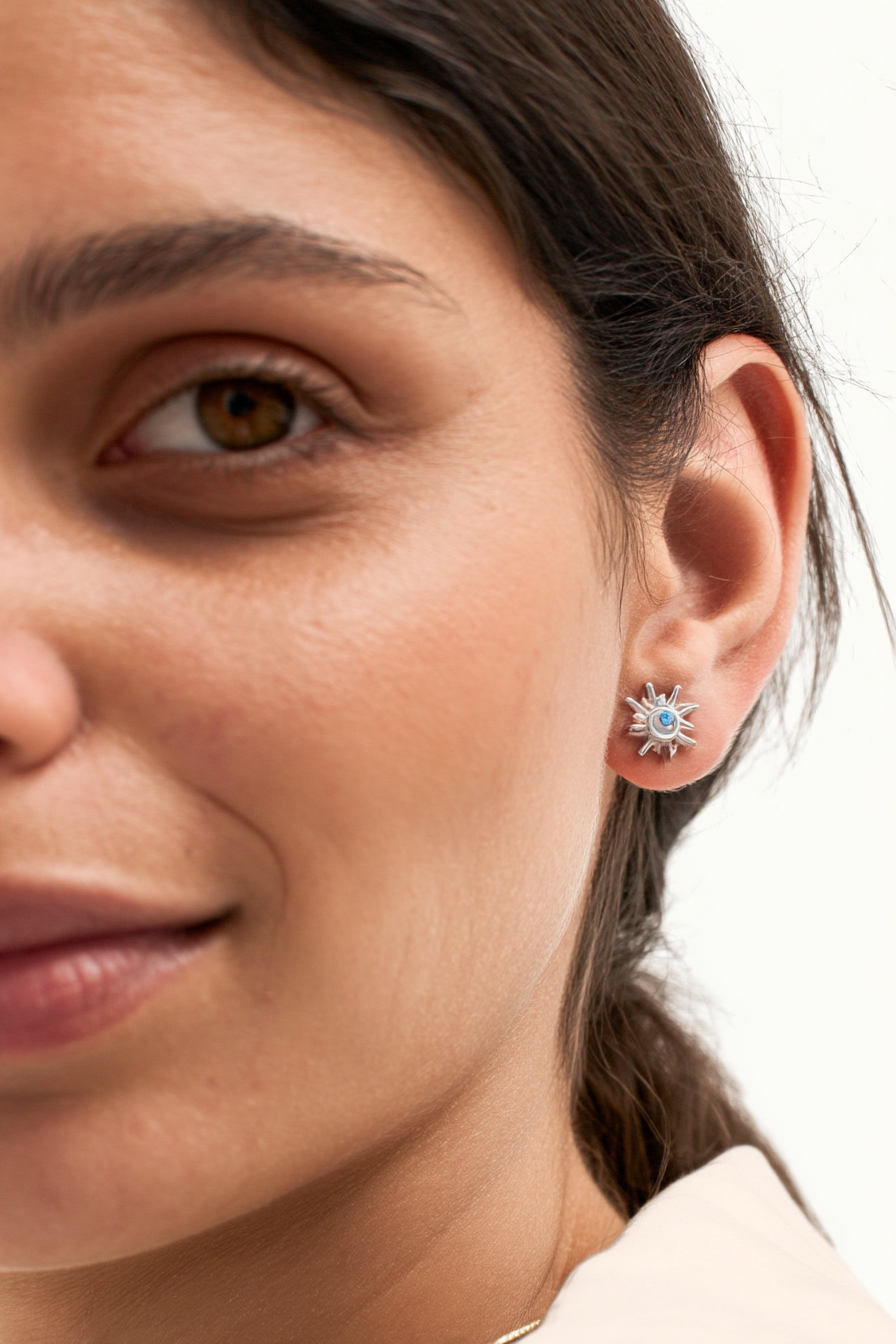 Macro shot of The Solis Azure Stud earrings, showcasing the sunburst silver design and a brilliant blue zircon center stone.