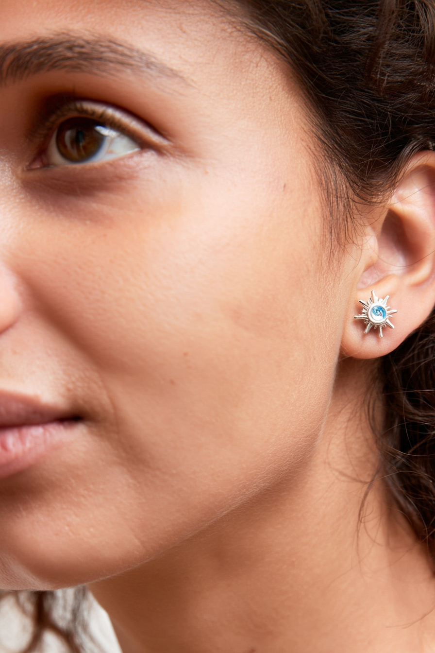 Macro shot of The Solis Azure Stud earrings, showcasing the sunburst silver design and a brilliant blue zircon center stone.