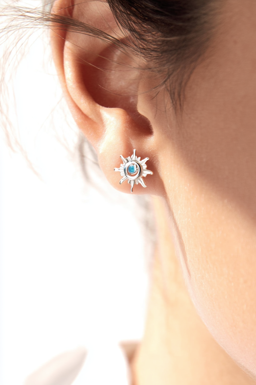 Macro shot of The Solis Azure Stud earrings, showcasing the sunburst silver design and a brilliant blue zircon center stone.