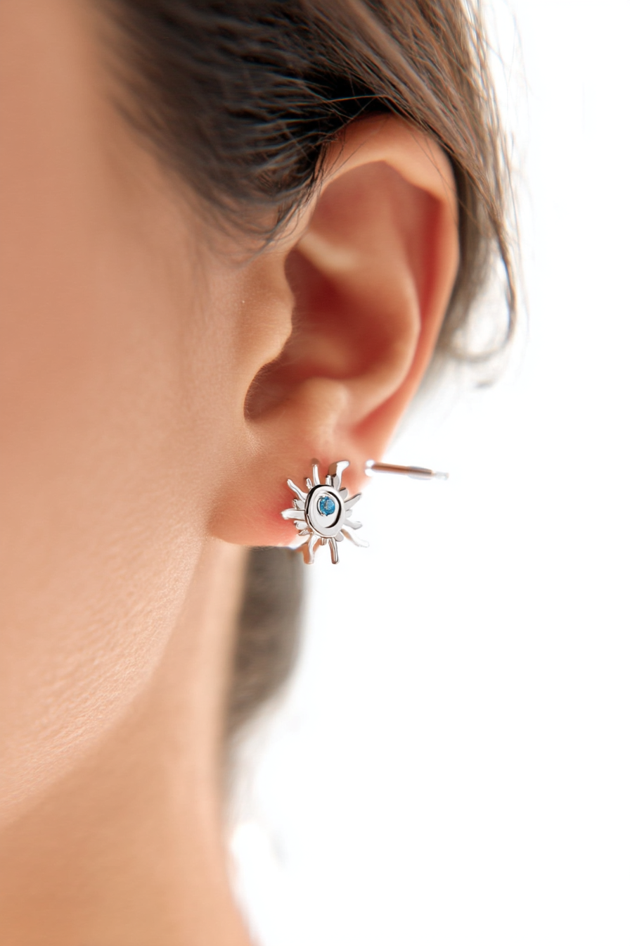 Macro shot of The Solis Azure Stud earrings, showcasing the sunburst silver design and a brilliant blue zircon center stone.