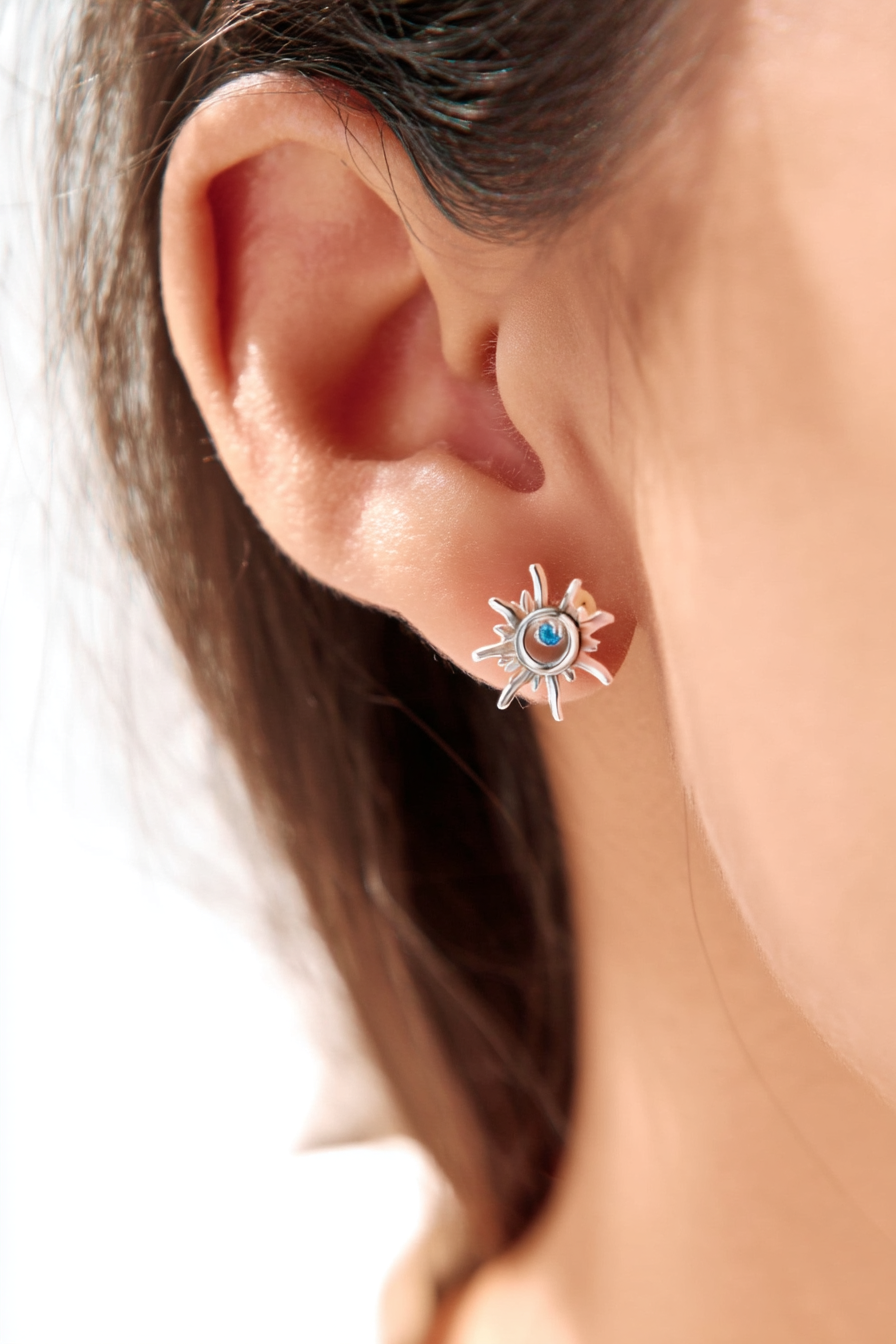 Macro shot of The Solis Azure Stud earrings, showcasing the sunburst silver design and a brilliant blue zircon center stone.