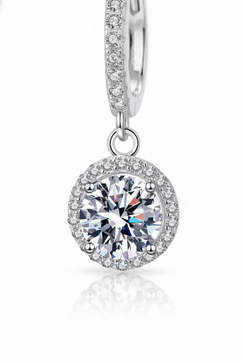 Close-up of The Stella drop earrings featuring a brilliant moissanite center stone in a round pavé halo, suspended from a silver huggie hoop.