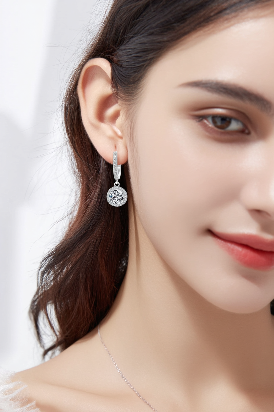 Close-up of The Stella drop earrings featuring a brilliant moissanite center stone in a round pavé halo, suspended from a silver huggie hoop.